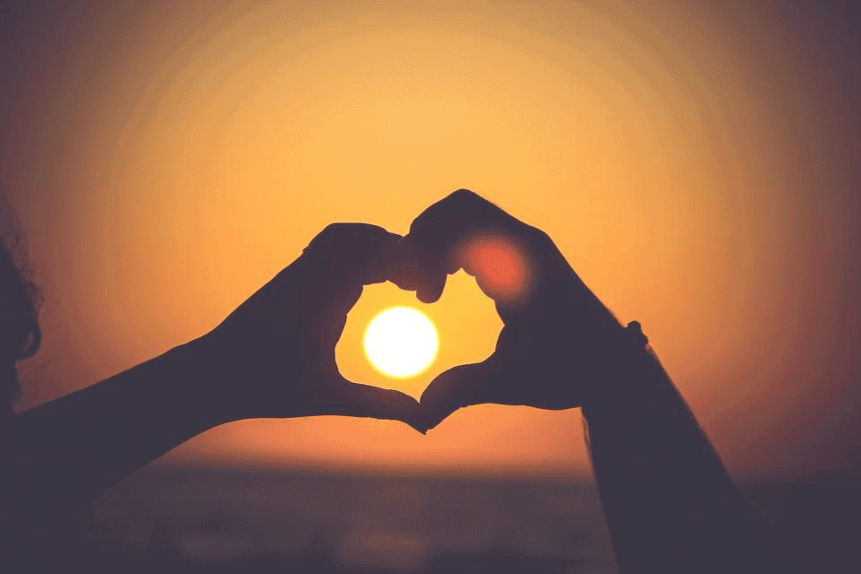 Hands in heart shape around setting sun