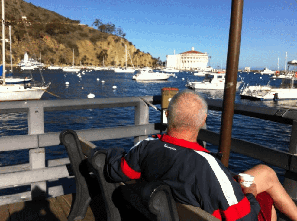 Sporty senior man with coffee on bench looking out over marina