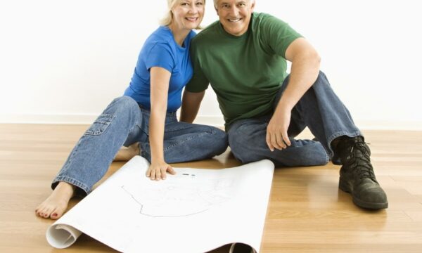 Photo of middle-aged couple sitting on floor with architectural blueprints