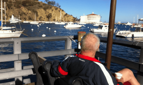 Sporty senior man with coffee on bench looking out over marina